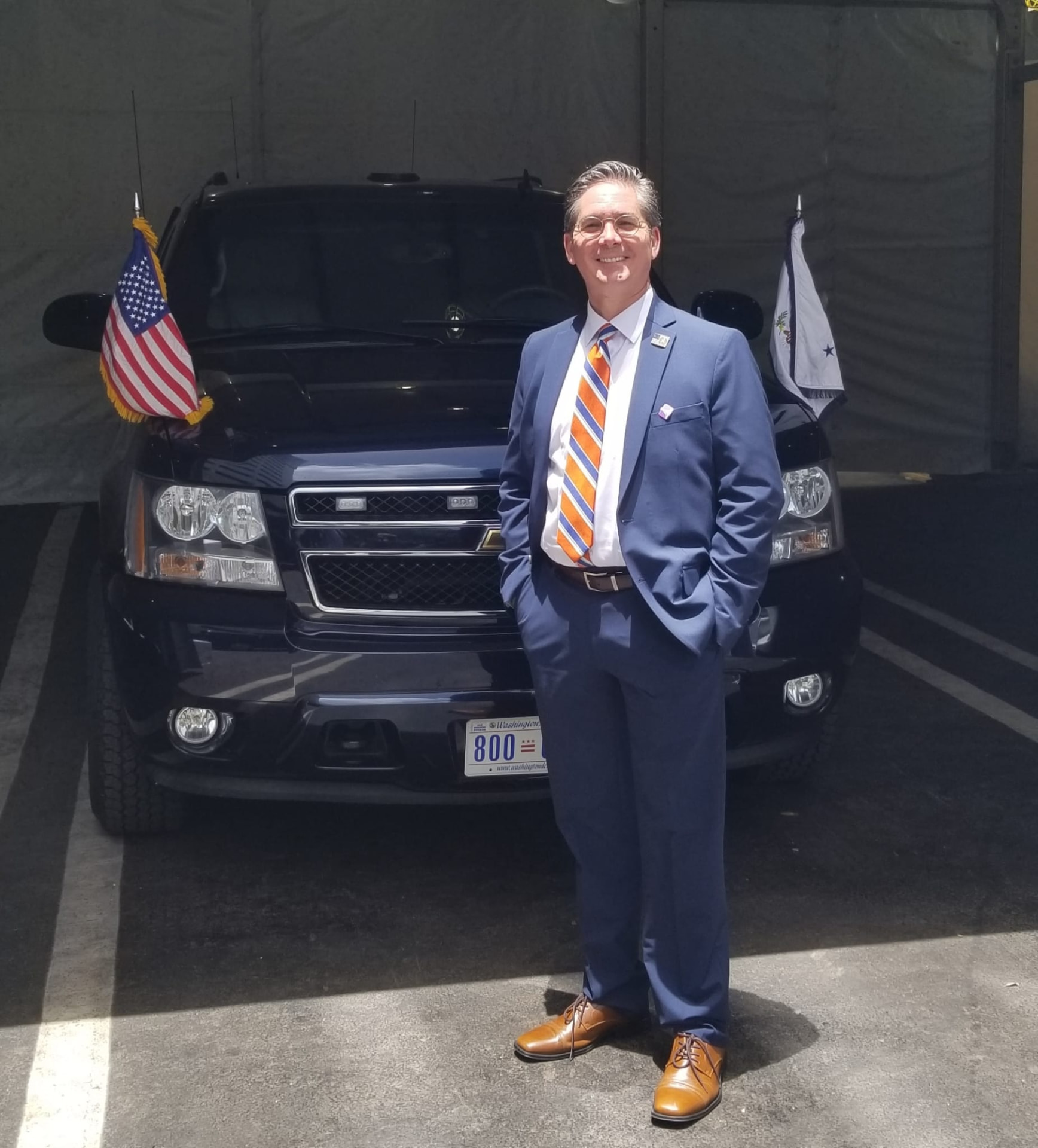 Kevin Hagen standing beside a government motorcade vehicle displaying United States and Vice Presidential flags