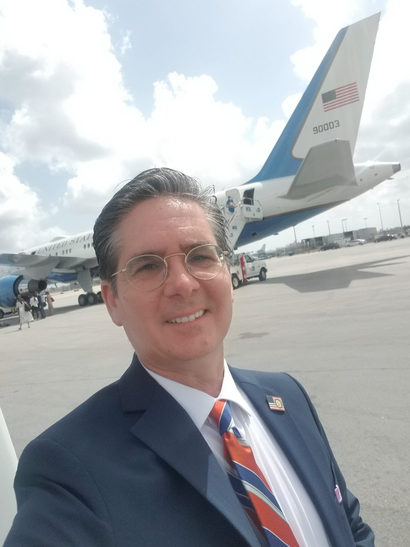 Kevin Hagen in a navy suit standing on an airport tarmac in front of a United States government aircraft